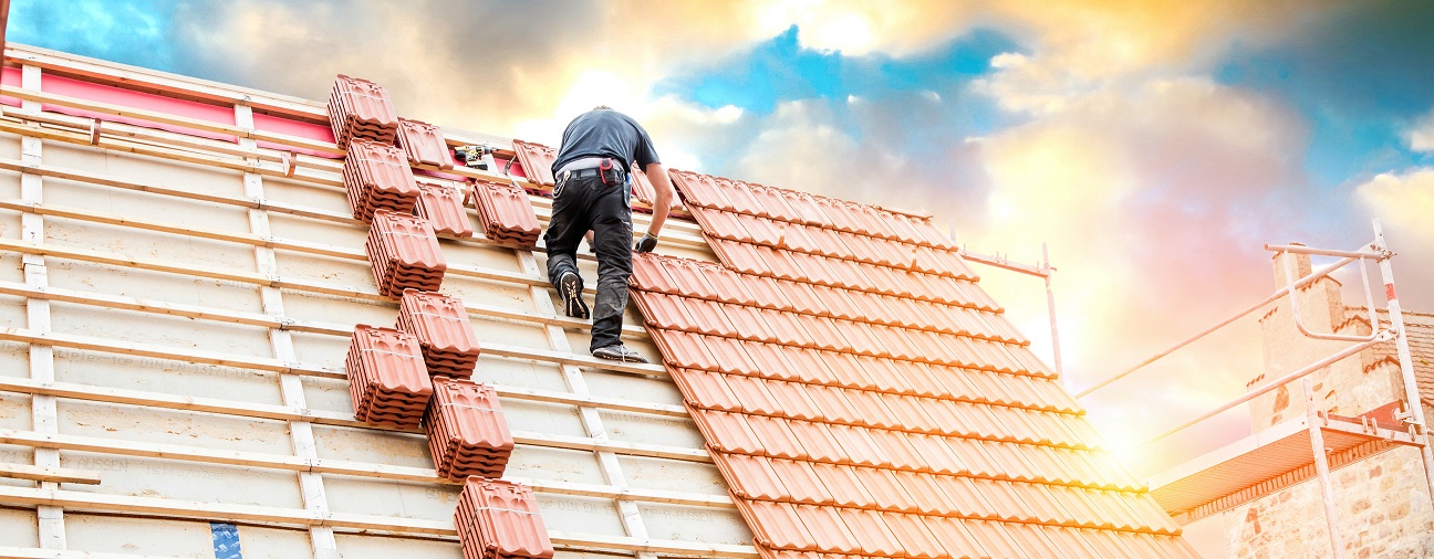 mężczyzna stojący na drewnianej konstrukcji dachowej wykonuje montaż i mocowanie dachówki ceramicznej
