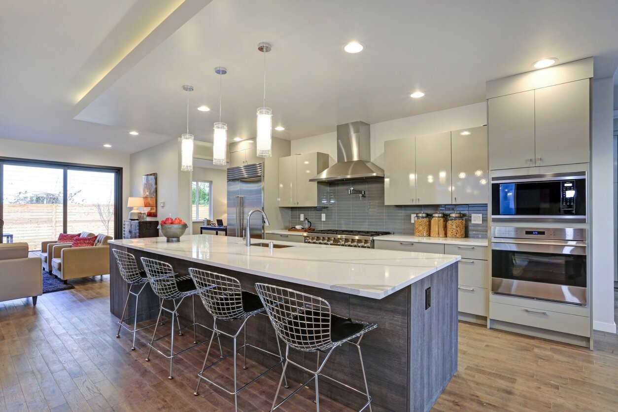 wnętrze nowoczesnej kuchni, połączonej z salonem, nad kuchenną wyspą zamontowany sufit podwieszany z oświetleniem LED